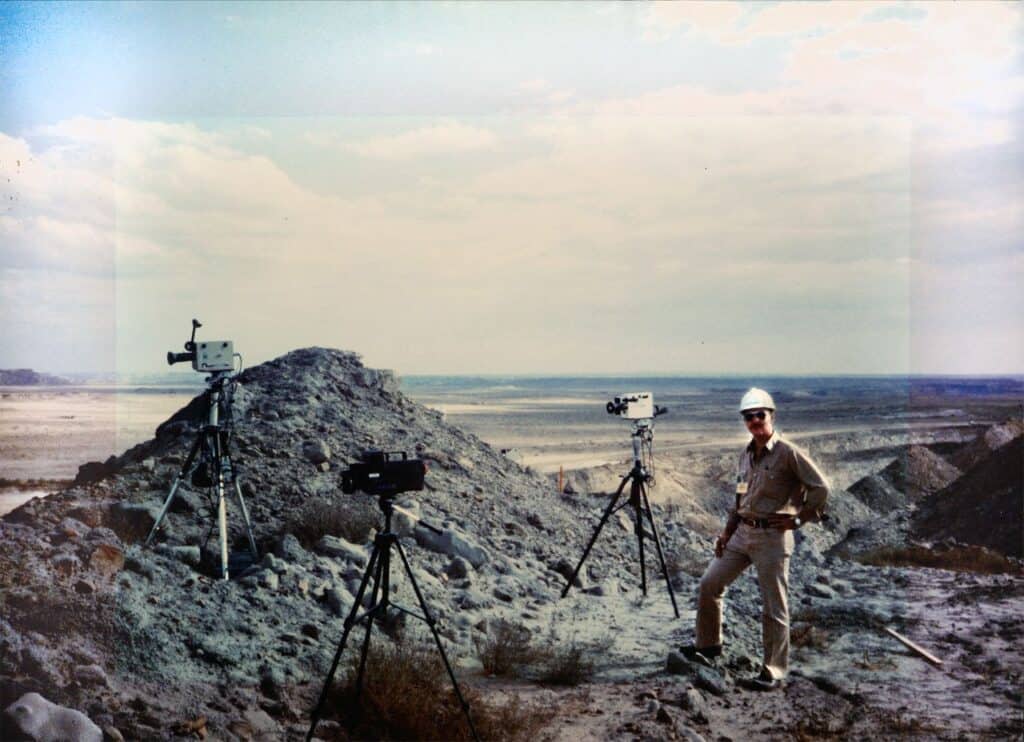 Tom Palangio with a hard hat on standing with cameras by a muckpile of rocks. Mining innovation